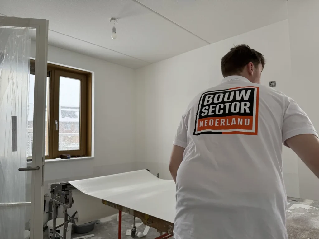 Behanger van Bouwsector Nederland rolt een baan wit vlies uit over de plaktafel in een lege slaapkamer