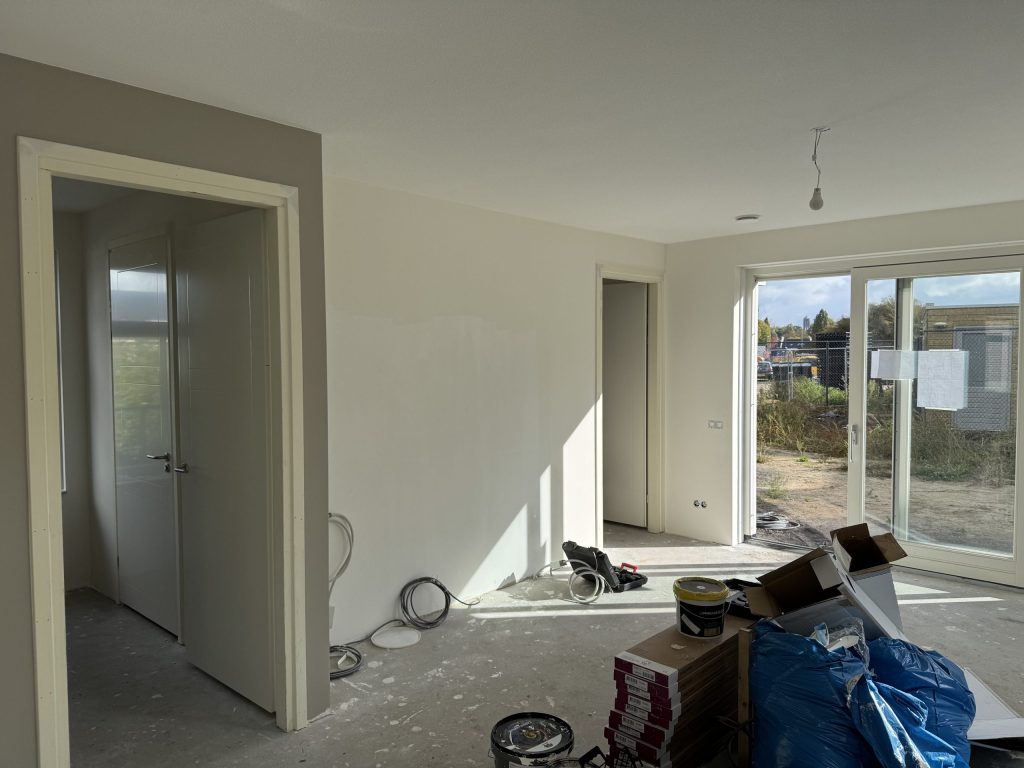 Woonkamer van een net opgeleverde eengezinswoning met kale wanden, tuindeuren en verfemmers op de vloer