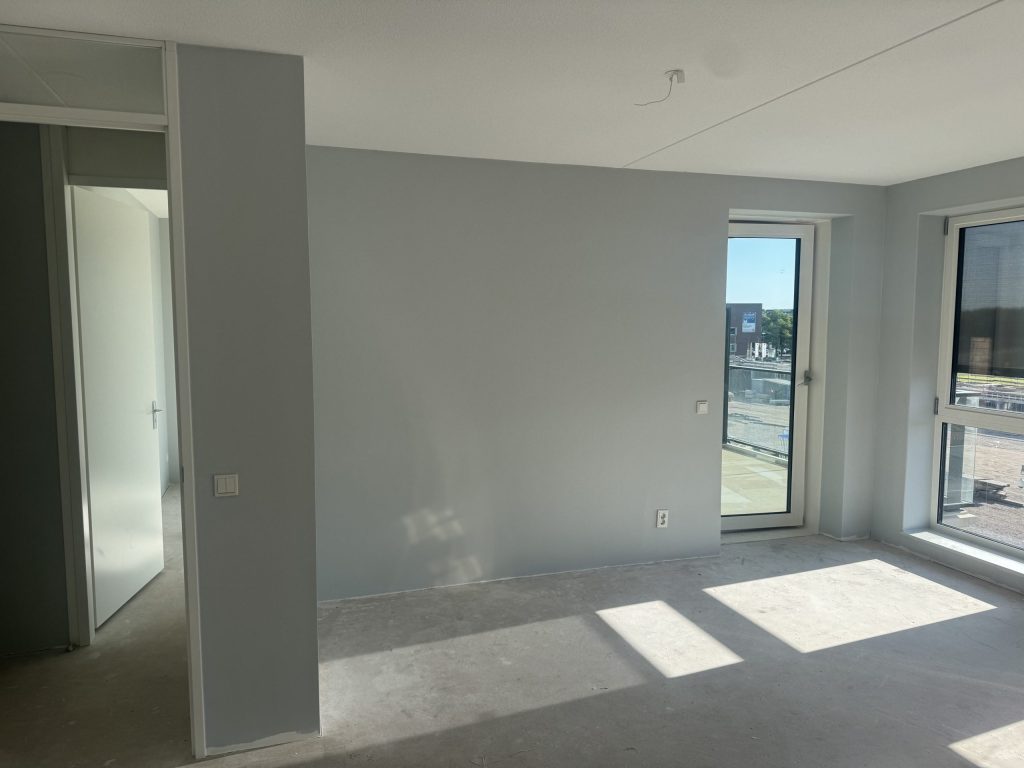 Appartement met lichtgrijze vlieswanden, een balkondeur en zon op de betonvloer