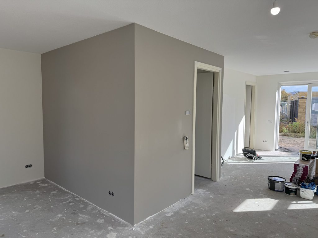 Nieuwbouwwoning met een grijs gesausde wand rond de meterkast en de tuindeuren open