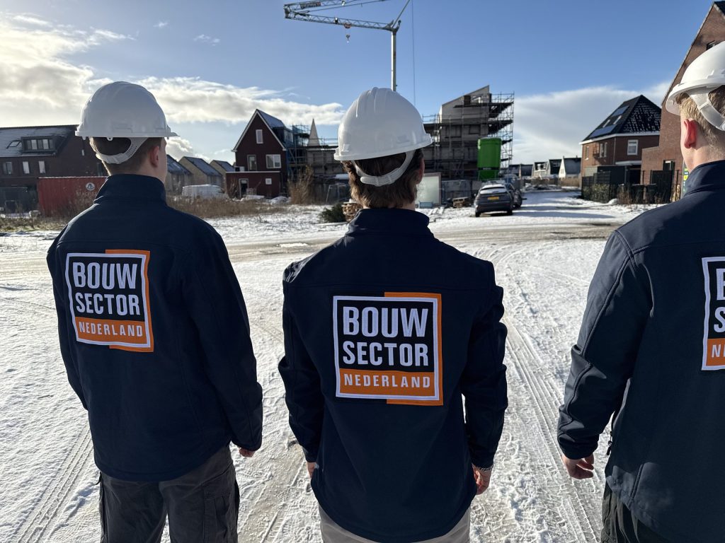 Drie medewerkers van Bouwsector Nederland in werkjas en helm op een besneeuwde nieuwbouwstraat