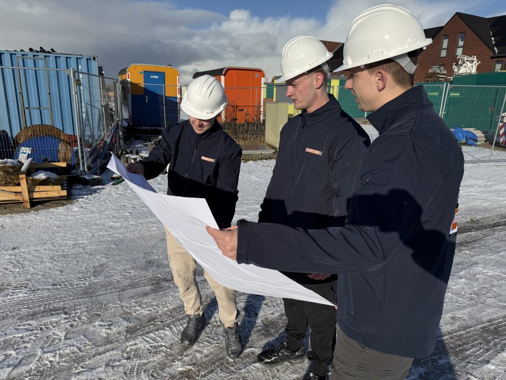 Drie vakmensen van Bouwsector Nederland met witte helm bekijken een bouwtekening op een winters bouwterrein