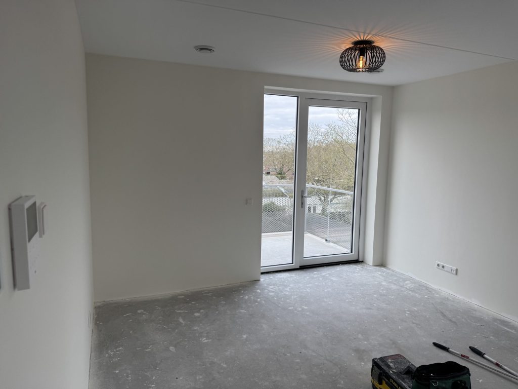 Nieuw appartement met gladde witte wanden, een balkondeur en een lamp aan het plafond, de vloer nog kaal