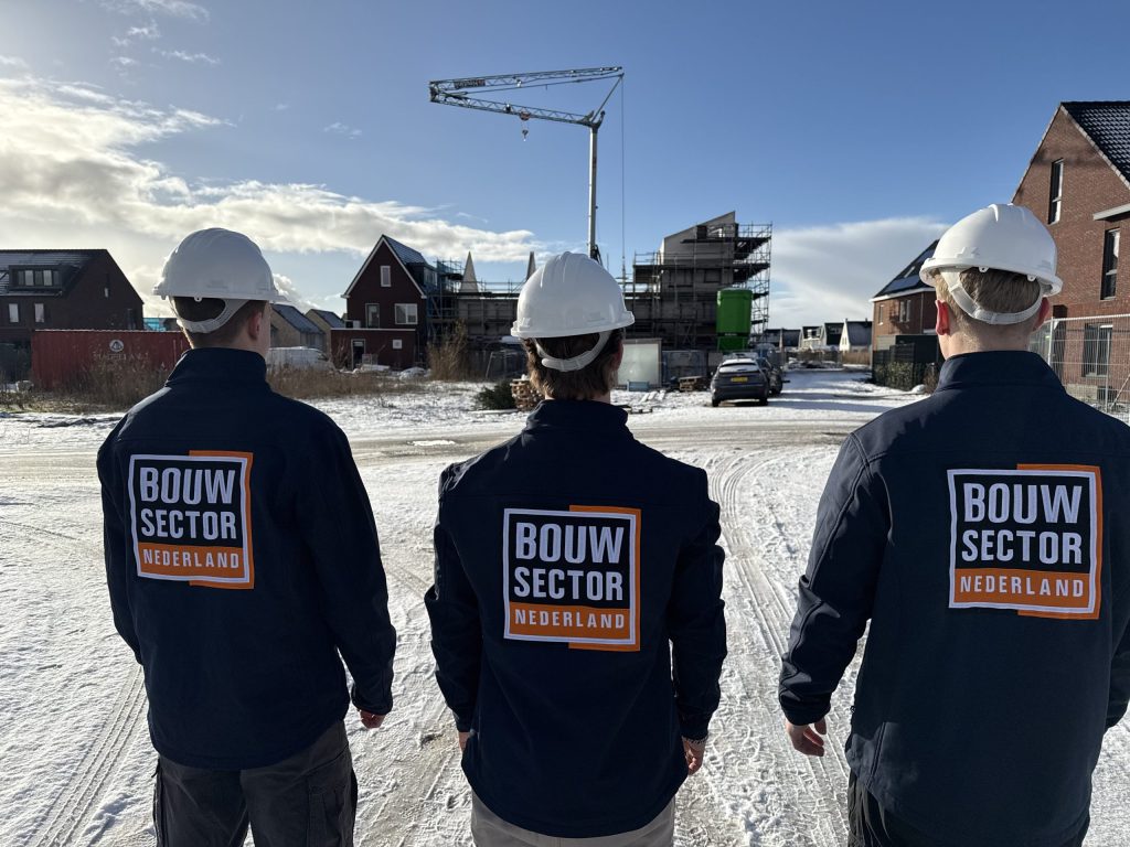 Drie vakmensen van Bouwsector Nederland met witte helm kijken naar nieuwbouwwoningen in aanbouw onder een winterlucht